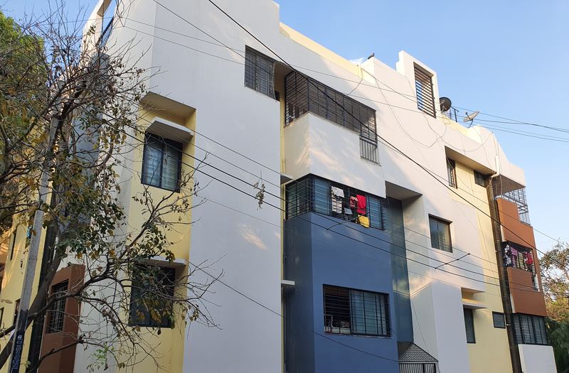 Completed white, blue and yellow apartment building on a tree-lined Bangalore street