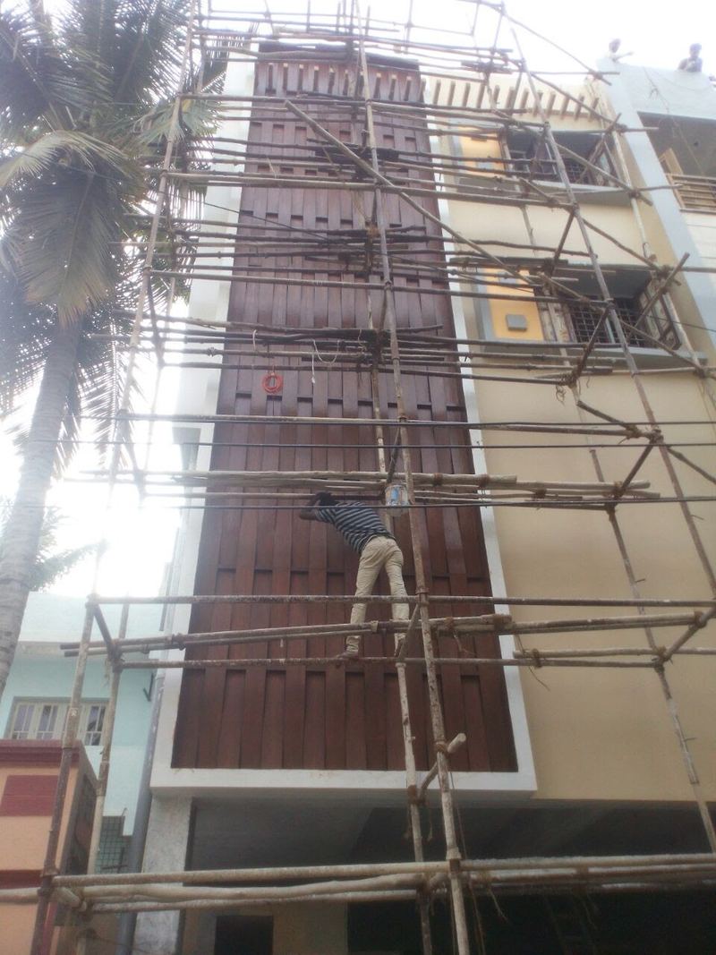 A worker on bamboo scaffolding fixing the wood-finish panels to the same wall