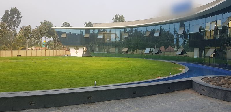 Curved glass façade of the campus building behind a lawn and a water channel