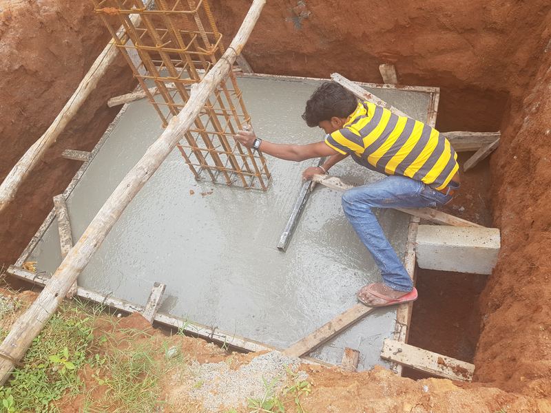 Worker levelling fresh concrete in a column footing, the column's reinforcement rising from it