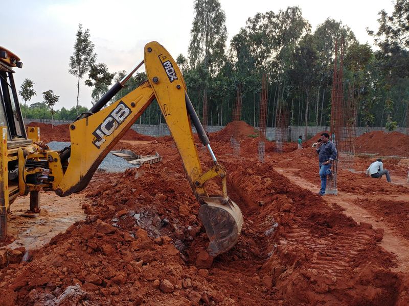 Excavator digging foundation trenches in red soil on an open site