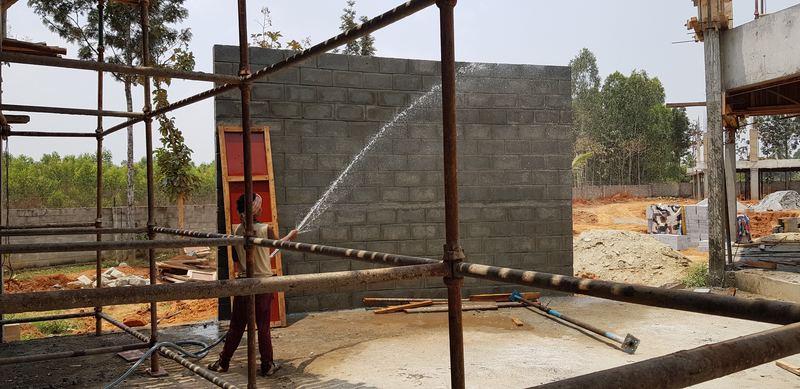 A new concrete-block wall being cured with a hose, behind scaffolding