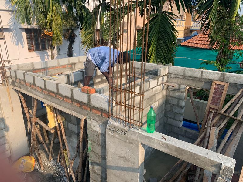 A mason laying concrete blocks beside column reinforcement on an upper floor