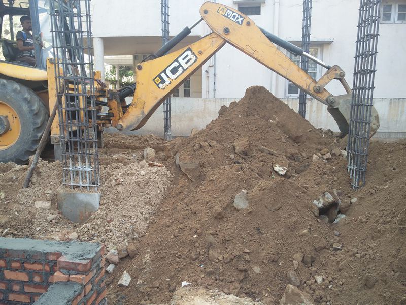 Backhoe loader digging between column reinforcement cages