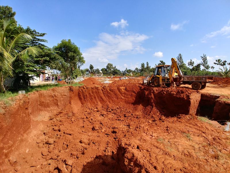 Excavator digging foundations on a red-soil site under a clear sky